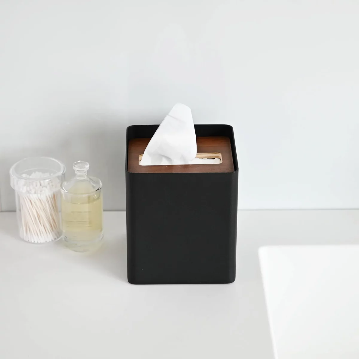 Yamazaki RIN Square Tissue Box in Black, on the shelf next to cotton swabs in a glass jar