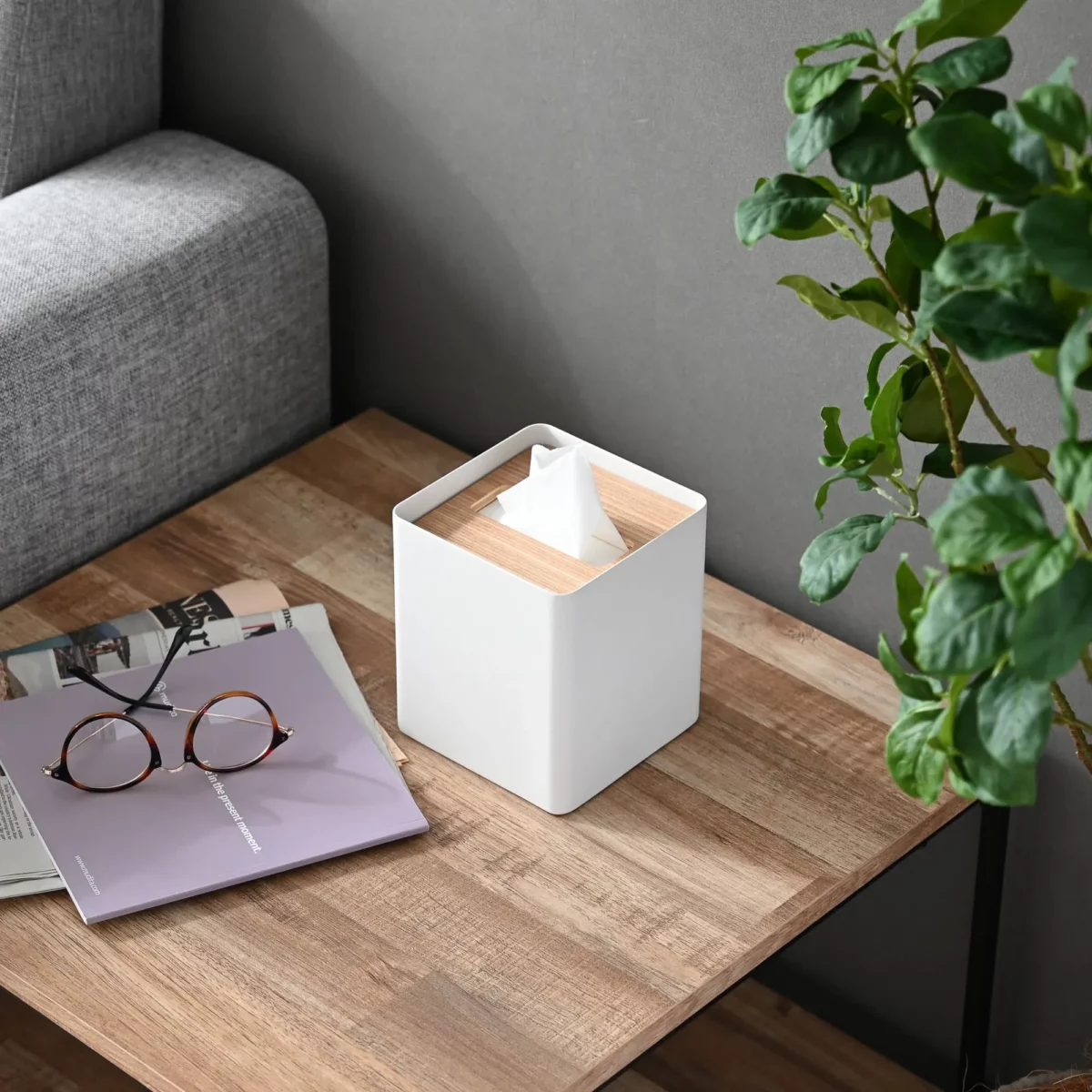 Yamazaki RIN square tissue box in white, on the wooden table next to glasses, a magazine, and a plant