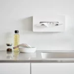 Boîte à mouchoirs Yamazaki TOWER avec crochets adhésifs, de couleur blanche, fixée à l'avant sur le mur de la cuisine, au-dessus du plan de travail