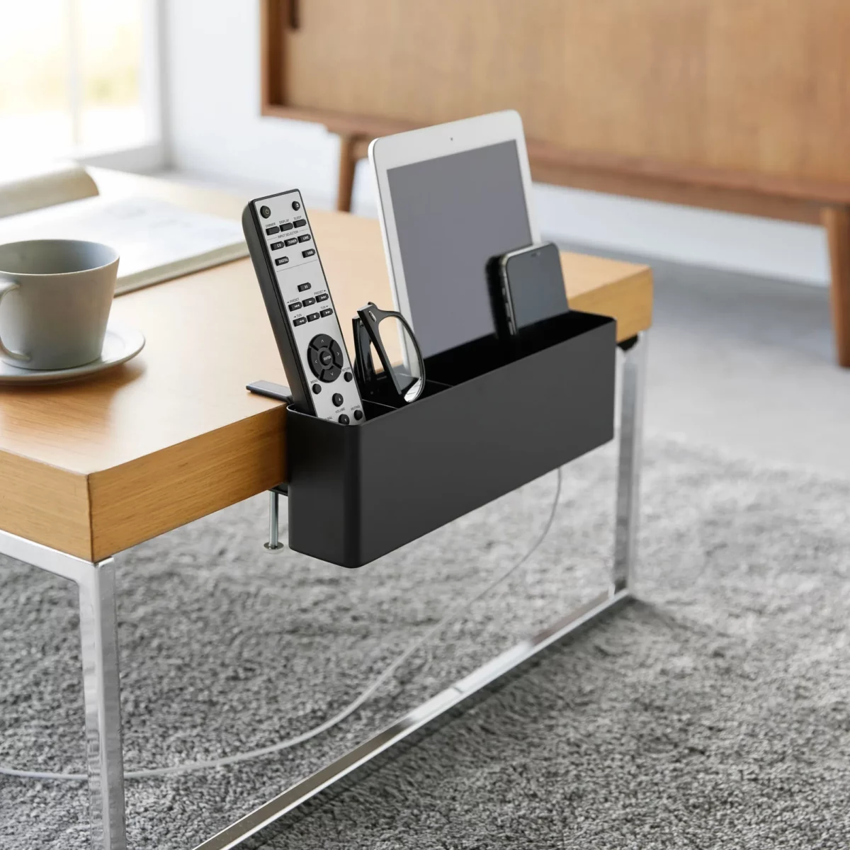 Yamazaki TOWER Narrow Table Clamp Basket in Black, on the coffee table with a remote control and tablet