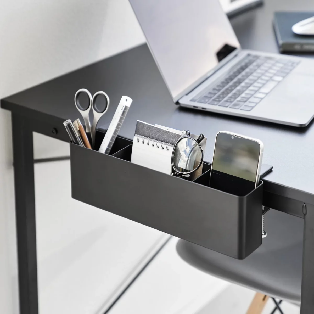 Yamazaki TOWER Narrow Table Clamp Basket in Black, on a desk with scissors, a notepad, and a smartphone