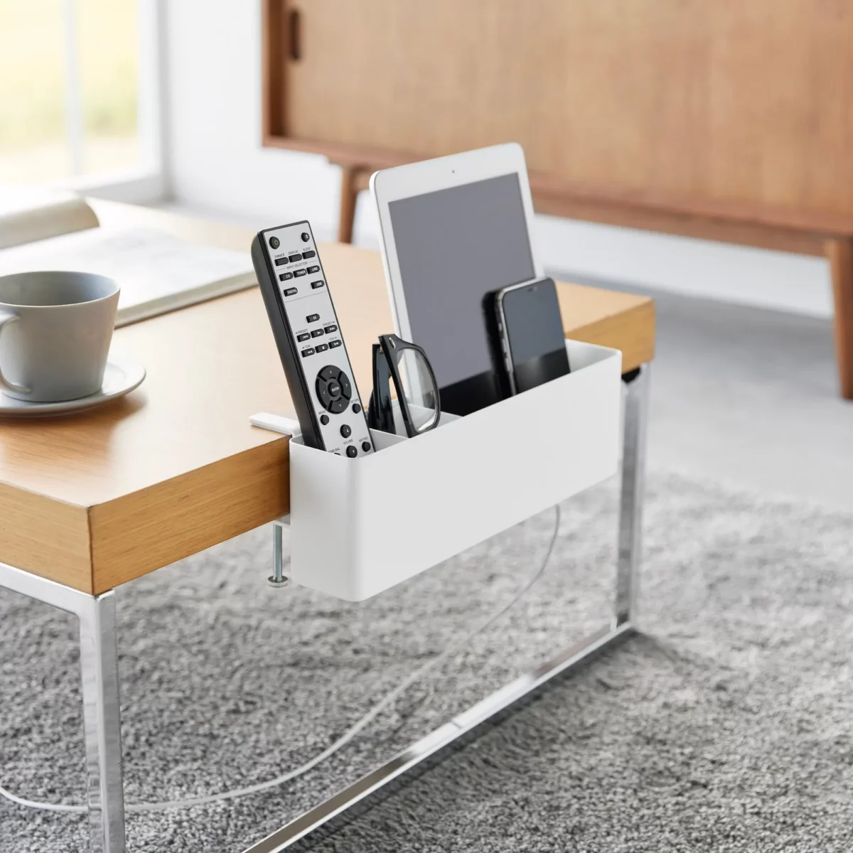 Yamazaki TOWER Narrow Table Clamp Basket in White, on a coffee table with a remote control and tablet