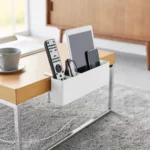 Yamazaki TOWER Narrow Table Clamp Basket in White, on a coffee table with a remote control and tablet