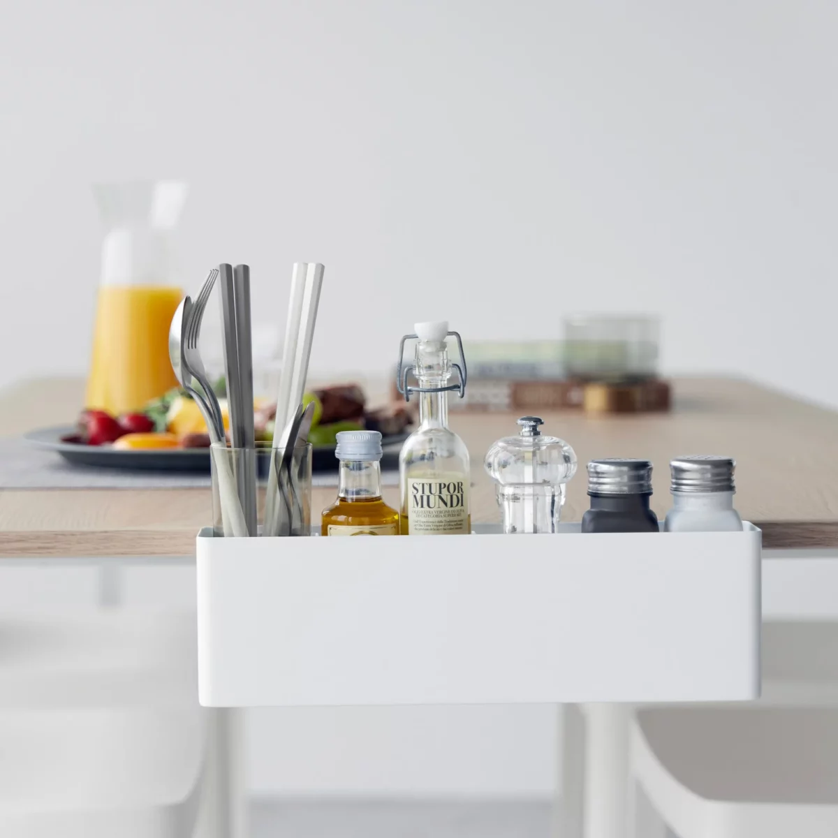 Yamazaki TOWER Narrow Table Clamp Basket in White, seen from the front at the breakfast table with silverware and juice