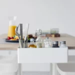 Yamazaki TOWER Narrow Table Clamp Basket in White, seen from the front at the breakfast table with silverware and juice