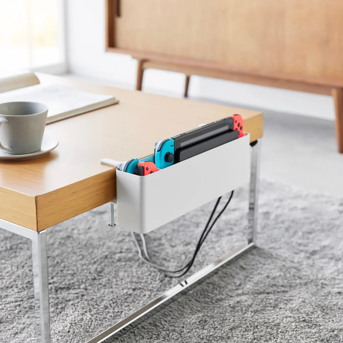 Yamazaki TOWER Narrow Table Clamp Basket in White, on a coffee table with a game console and charging cable