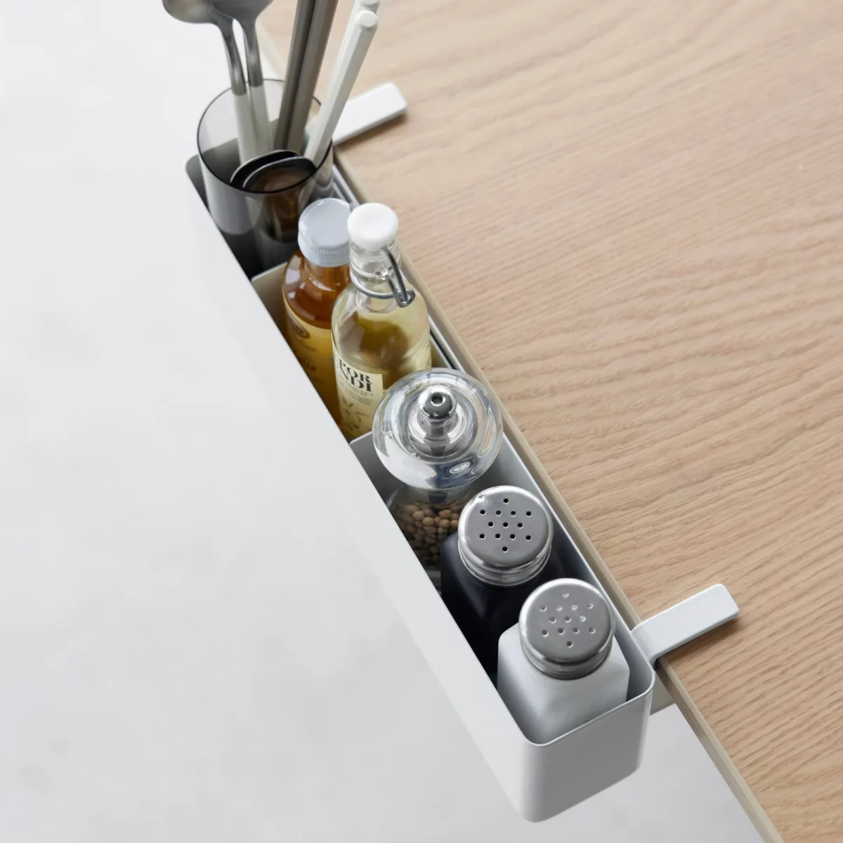 Yamazaki TOWER Narrow Table Clamp Basket in White, viewed from above along the edge of the table with spice jars