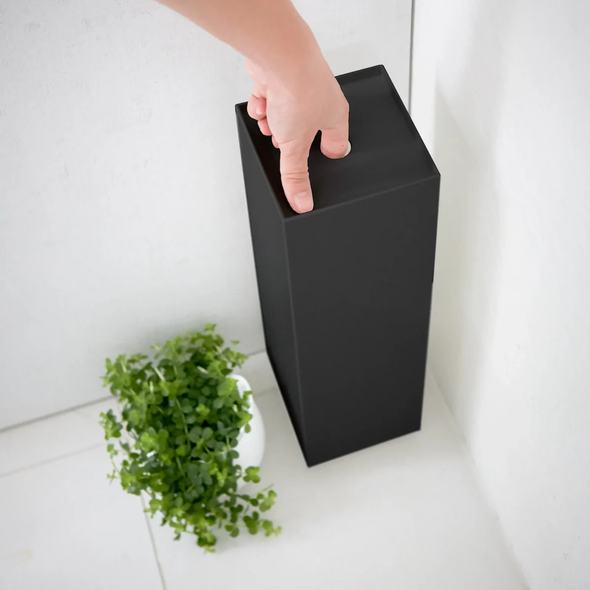 Porte-papier hygiénique Yamazaki TOWER, modèle étroit, noir ; la main tient le porte-papier par le trou de préhension