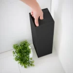 Porte-papier hygiénique Yamazaki TOWER, modèle étroit, noir ; la main tient le porte-papier par le trou de préhension