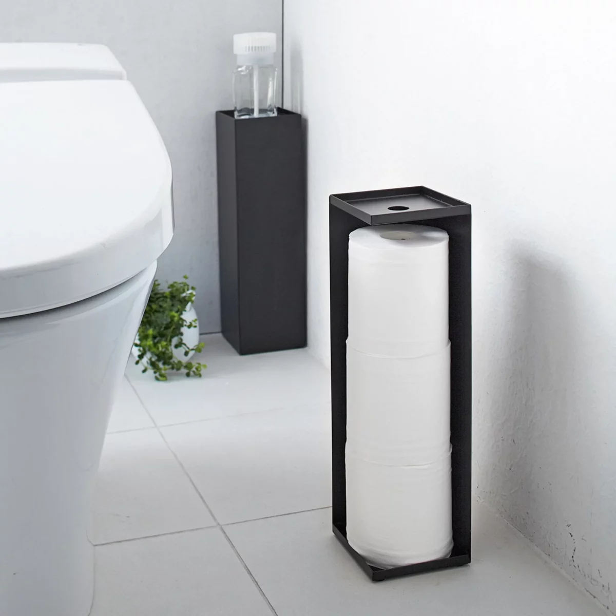 Porte-papier toilette Yamazaki TOWER, modèle étroit, noir, placé à l'avant, à côté des toilettes, avec les rouleaux visibles
