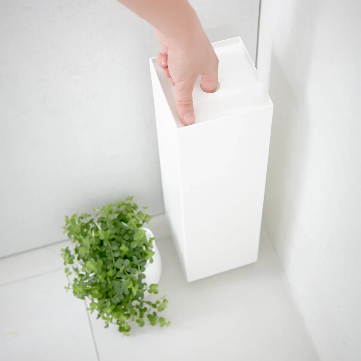 Porte-papier hygiénique Yamazaki TOWER, modèle étroit, blanc ; la main tient le porte-papier par le trou de préhension