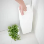 Porte-papier hygiénique Yamazaki TOWER, modèle étroit, blanc ; la main tient le porte-papier par le trou de préhension