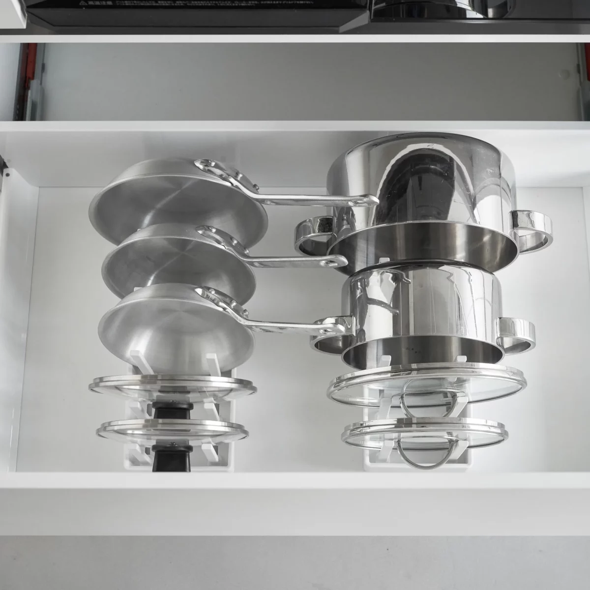 Organiseur de casseroles et de couvercles Yamazaki « TOWER », réglable, blanc, vu d'en haut avec des casseroles empilées dans le tiroir