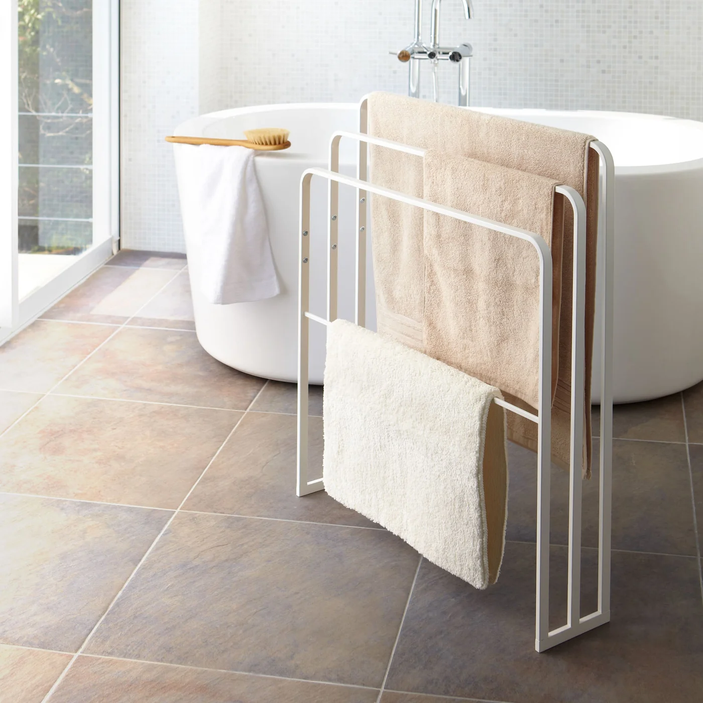 Yamazaki TOWER Badetuch-Halter mit drei Handtüchern und Badematte neben einer Badewanne