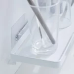 Étagère murale TOWER de Yamazaki avec crochets adhésifs, couleur blanche ; gros plan avec un verre posé sur la grille