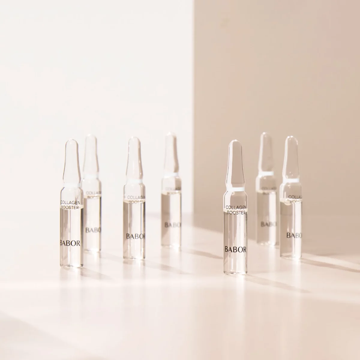 Mehrere BABOR Collagen Booster Ampullen stehen im warmen Licht auf einer hellen Fläche, Stimmungsbild
