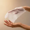 Ein BABOR Oil Infused Cleansing Wipe schwebt über einer offenen Hand, das Reinigungstuch im Einsatz