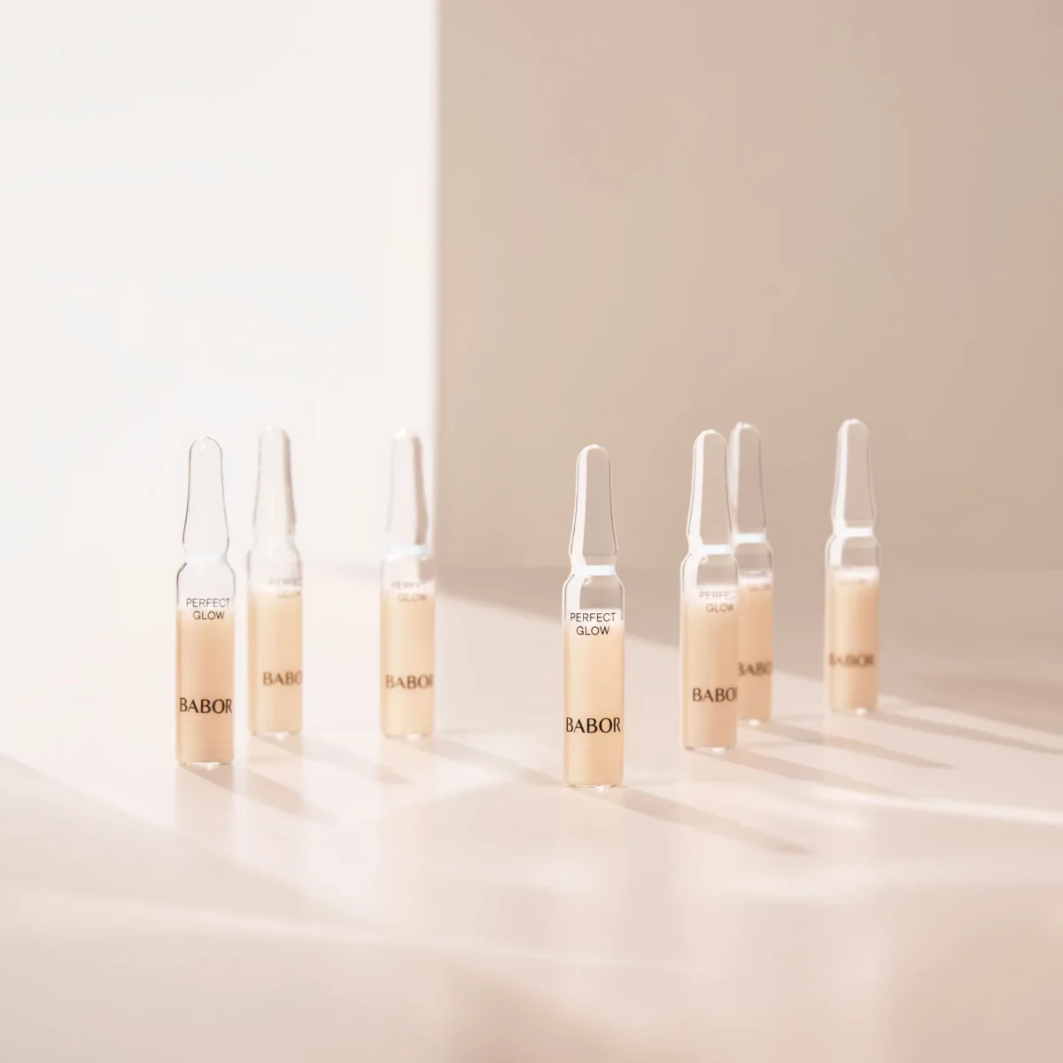 Mehrere BABOR Perfect Glow Ampullen stehen im warmen Sonnenlicht auf einer hellen Fläche, Stimmungsbild