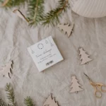 Eulenschnitt wooden fir tree ornament in natural finish, arranged on linen, with packaging, a fir branch, and gold scissors