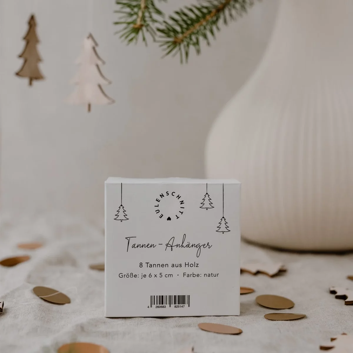 Packaging for the Eulenschnitt wooden fir tree pendants (set of 8) in natural finish, set against a vase with wooden fir trees hanging above it