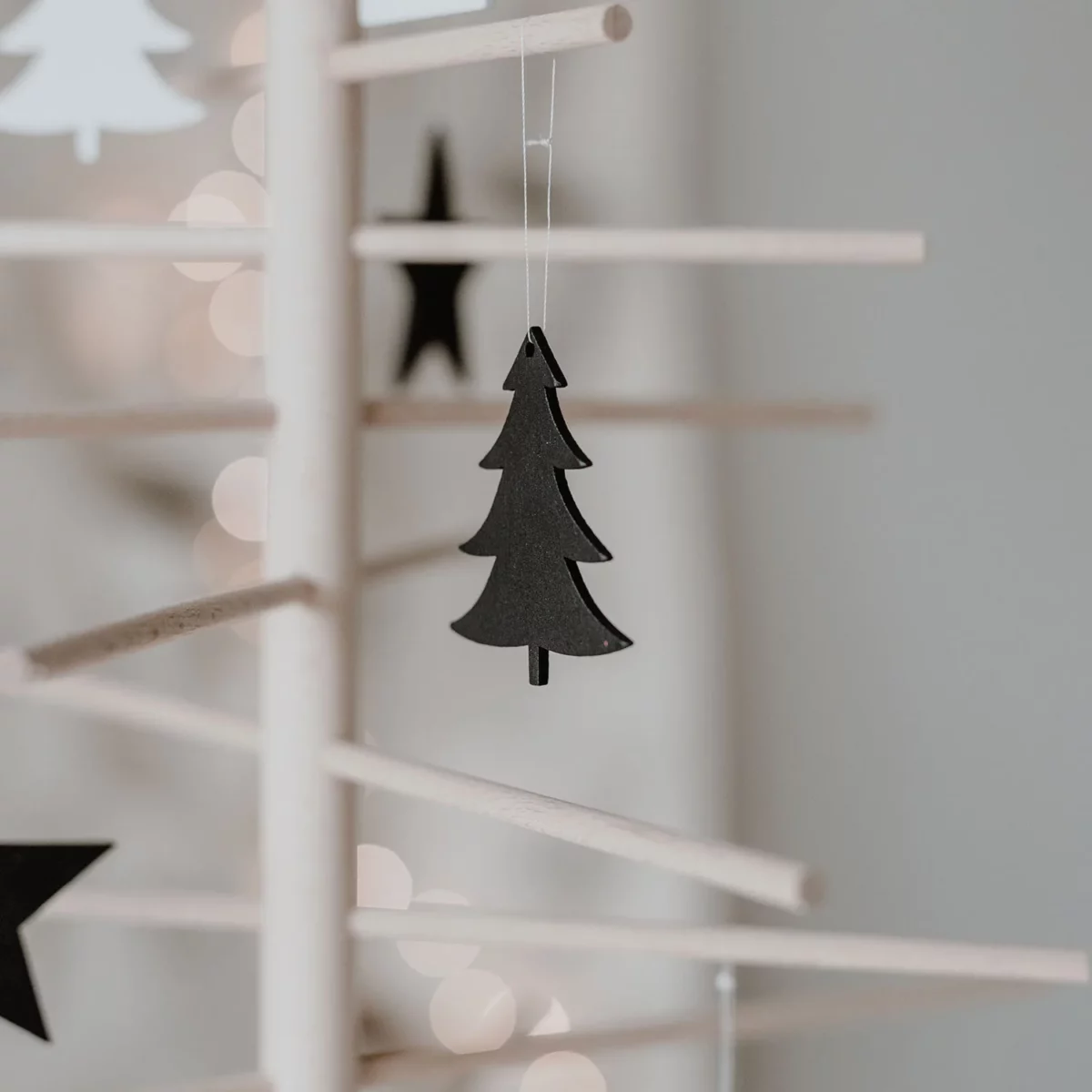 Eulenschnitt wooden fir tree ornament in black on a decorative tree made of wooden sticks, with stars and candlelight in the background
