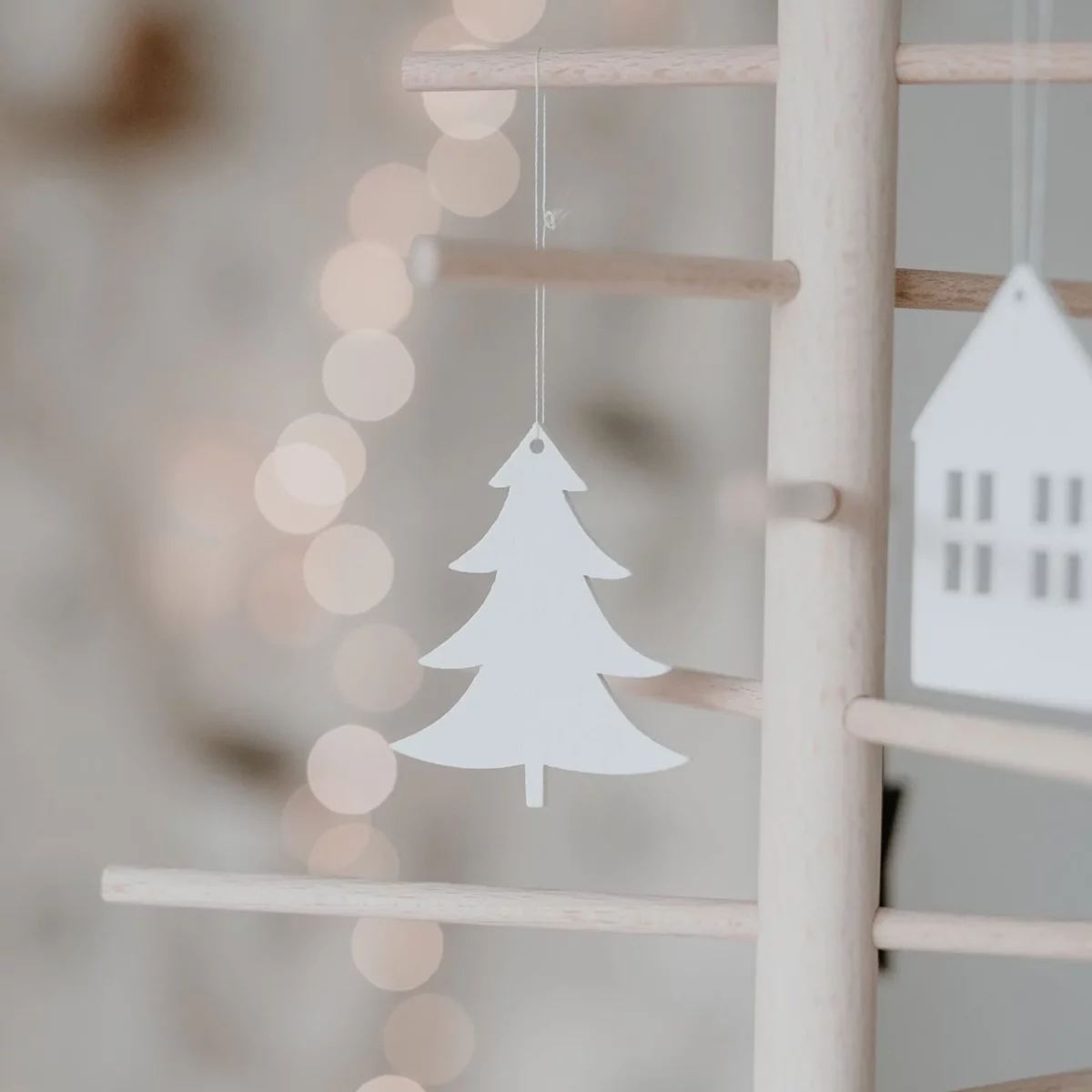 Eulenschnitt wooden ornament: a white fir tree on a wooden stick decorative tree next to a white house, with lights in the background
