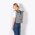 Femme portant le sac à dos Ucon Acrobatics Hajo Medium Stealth gris, vue de profil avec le rolltop fermé