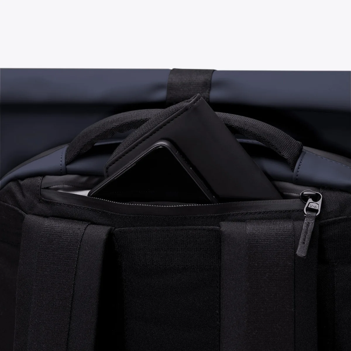 Pocket at the top of the back panel of the Ucon Acrobatics Hajo Pro backpack in dark navy holding a phone and wallet