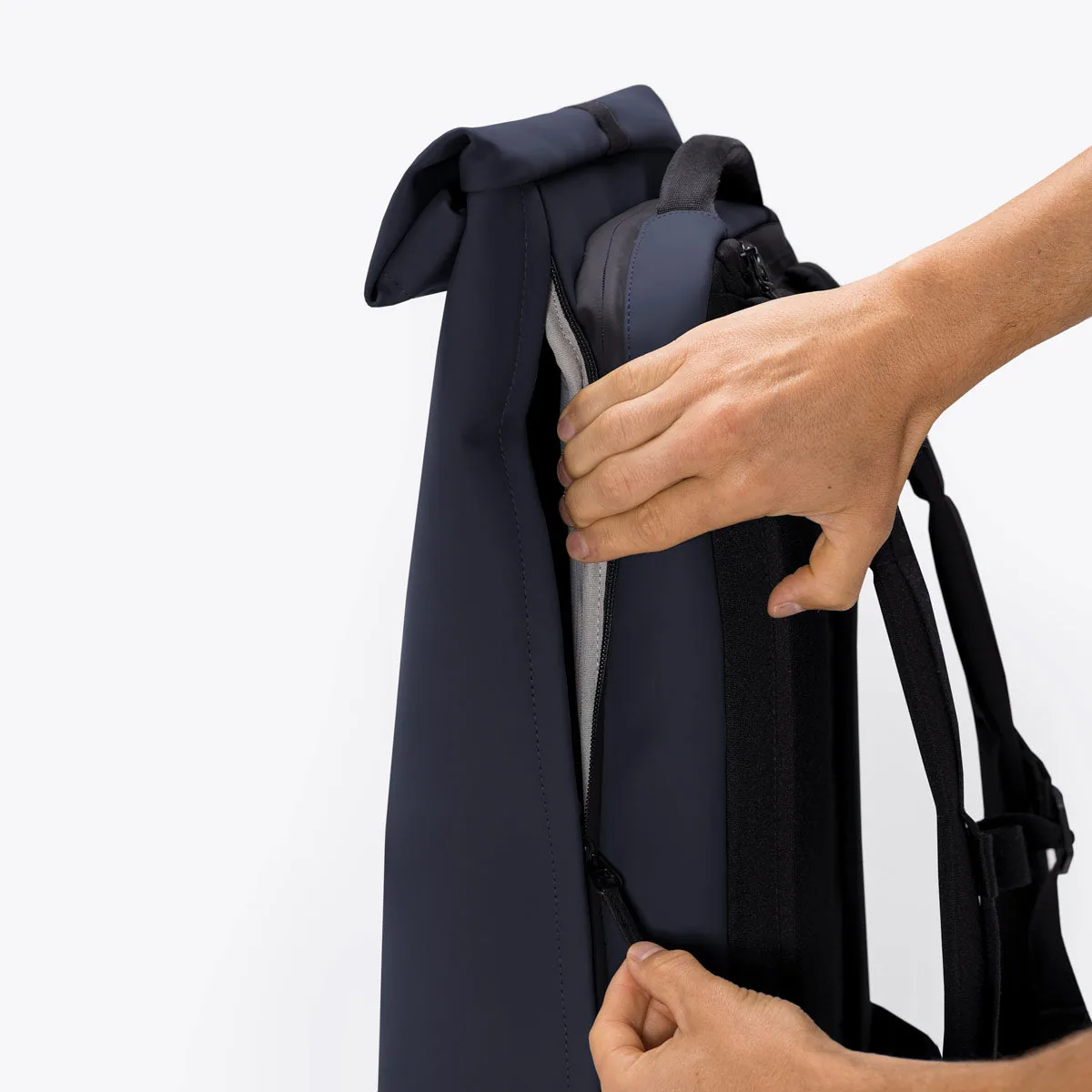 Hands opening the side zip of the Ucon Acrobatics Hajo Pro in dark navy to reach the main compartment without unrolling