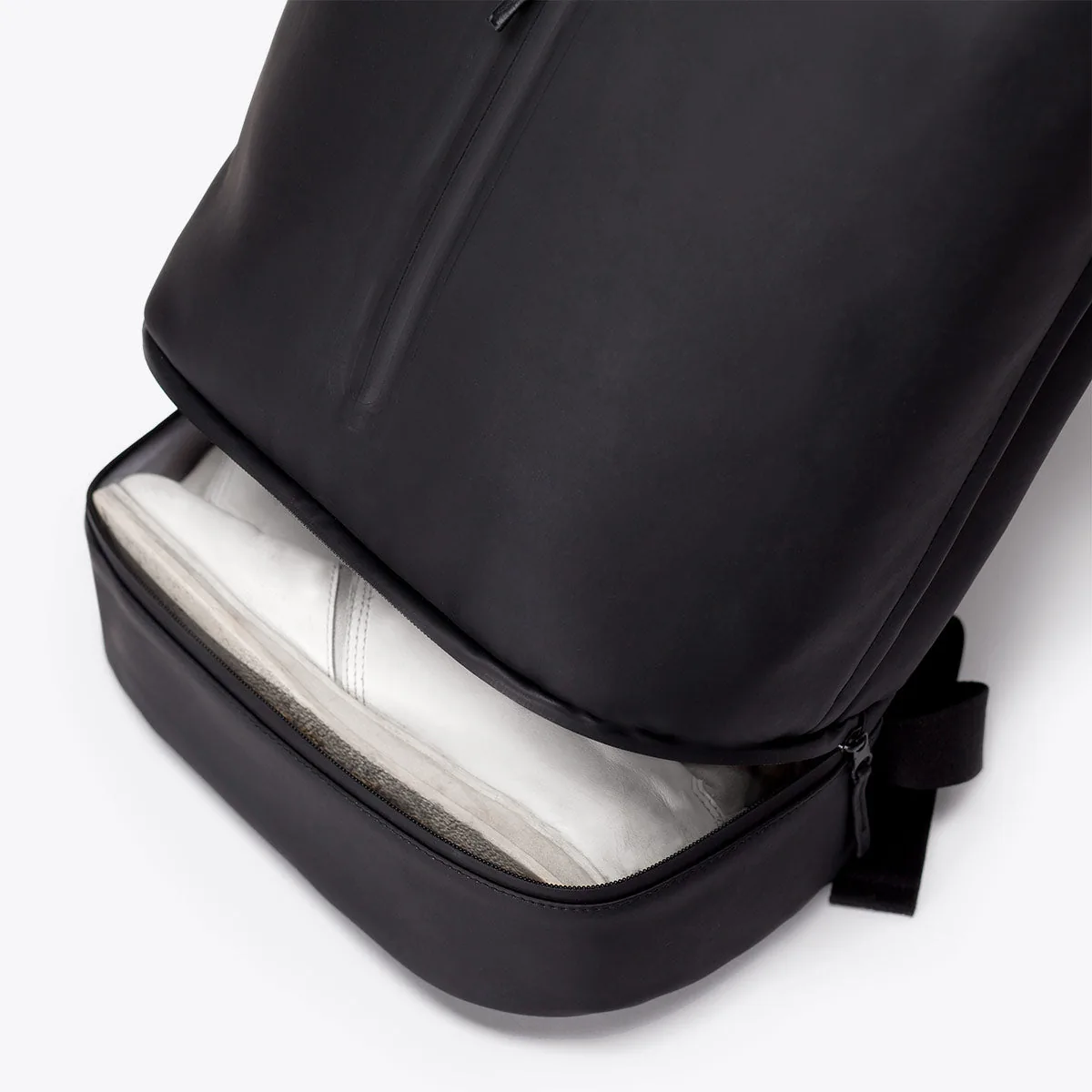 Open bottom compartment of the Ucon Acrobatics Hajo Pro backpack in black holding a sneaker, apart from the main bag