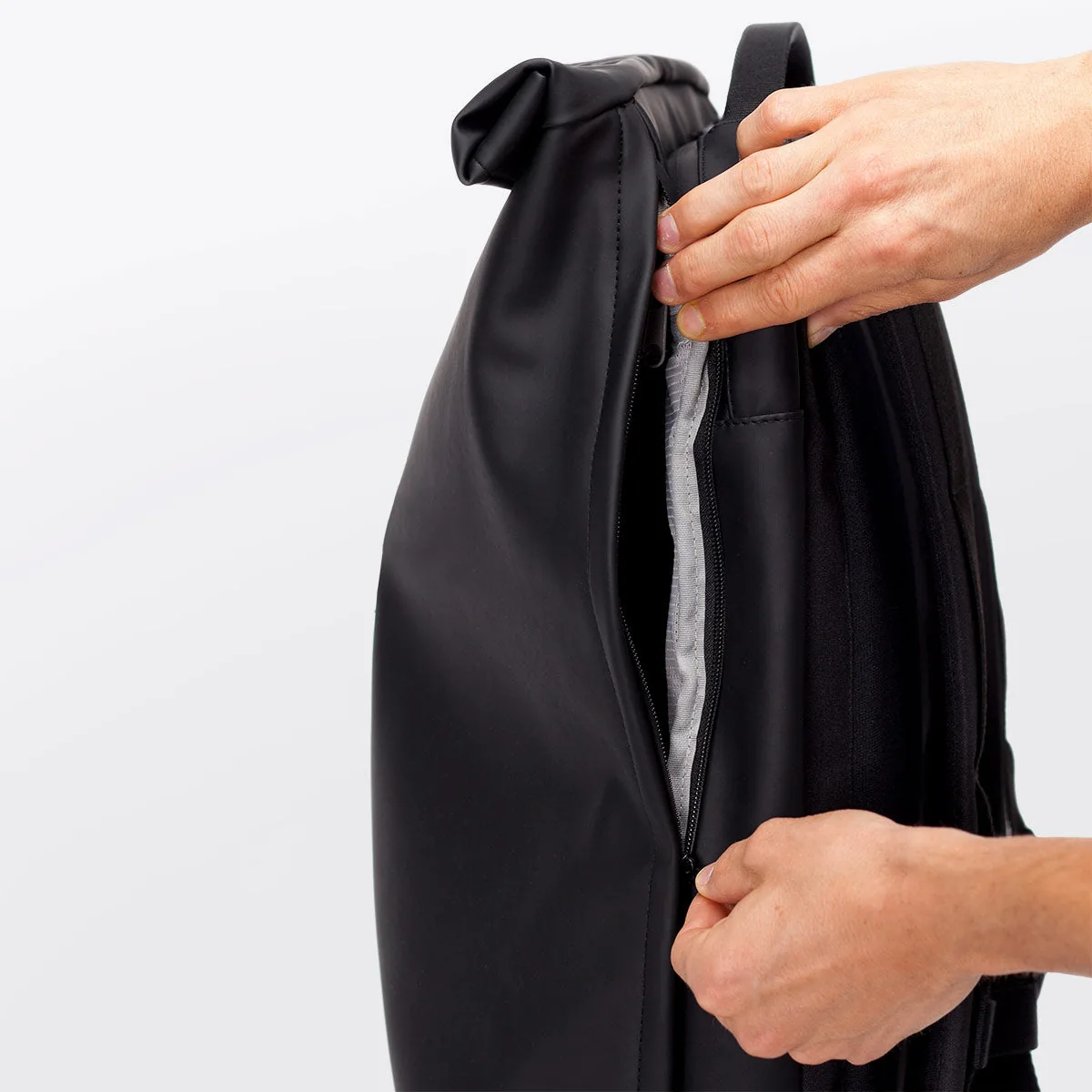 Hands opening the side zip of the Ucon Acrobatics Hajo Pro in black to reach the main compartment without unrolling