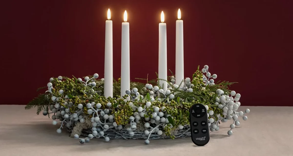 Uyuni Oval Remote Control in black on the table in front of a wreath with four glowing Uyuni LED taper candles
