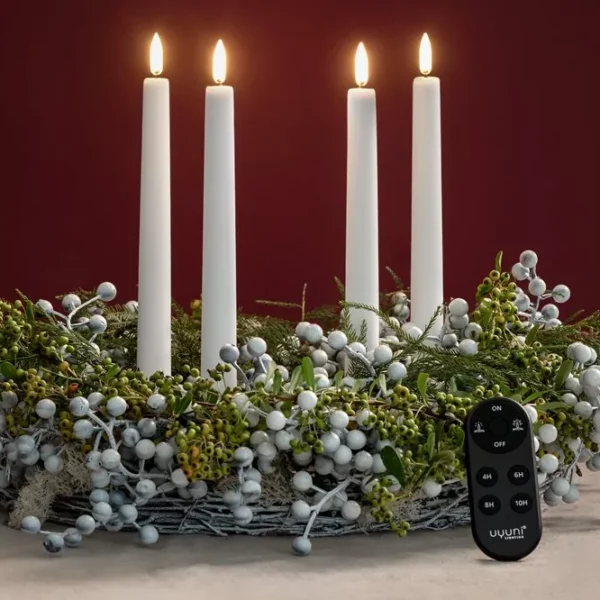Télécommande Uyuni ovale, de couleur noire, posée sur la table devant une couronne composée de quatre bougies cylindriques à LED lumineuses de la marque Uyuni